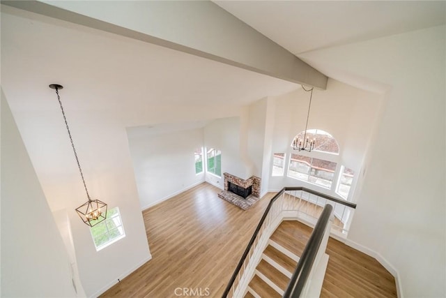 hall with beam ceiling, an upstairs landing, wood finished floors, a chandelier, and baseboards