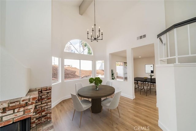 dining space with a towering ceiling, visible vents, baseboards, light wood finished floors, and an inviting chandelier