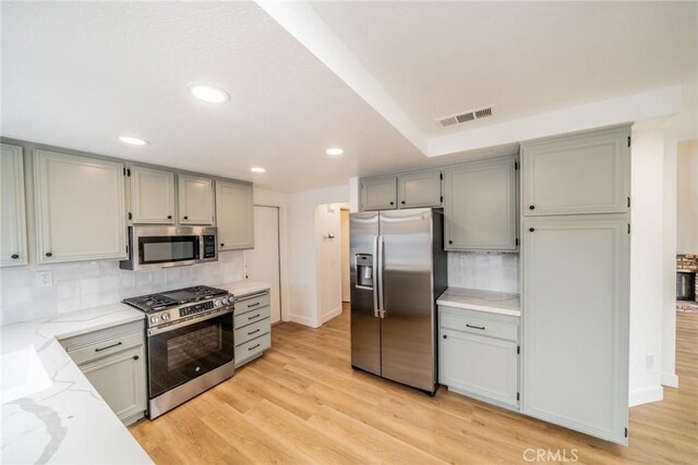 kitchen featuring light wood finished floors, visible vents, decorative backsplash, appliances with stainless steel finishes, and light stone countertops