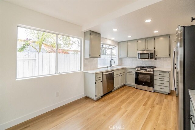 kitchen featuring stainless steel appliances, baseboards, light countertops, light wood-type flooring, and backsplash