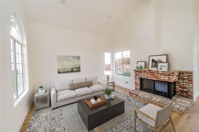 living area with a brick fireplace, high vaulted ceiling, and wood finished floors