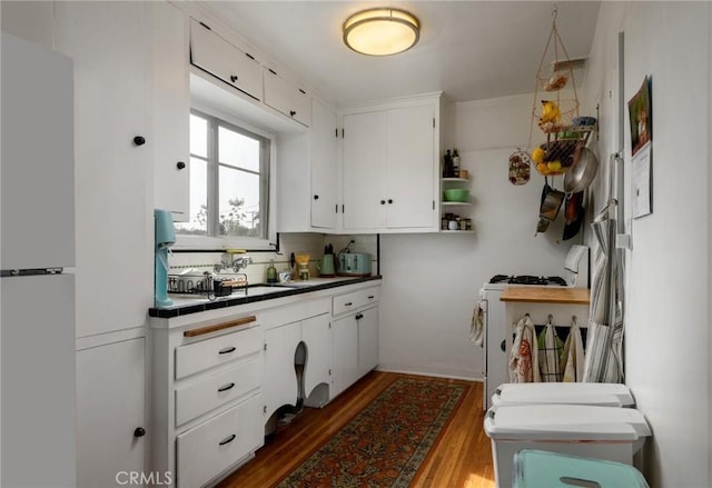 kitchen featuring wood finished floors, white cabinets, freestanding refrigerator, open shelves, and range with gas cooktop