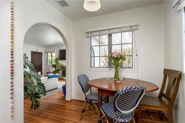 dining space with arched walkways, wood finished floors, and visible vents