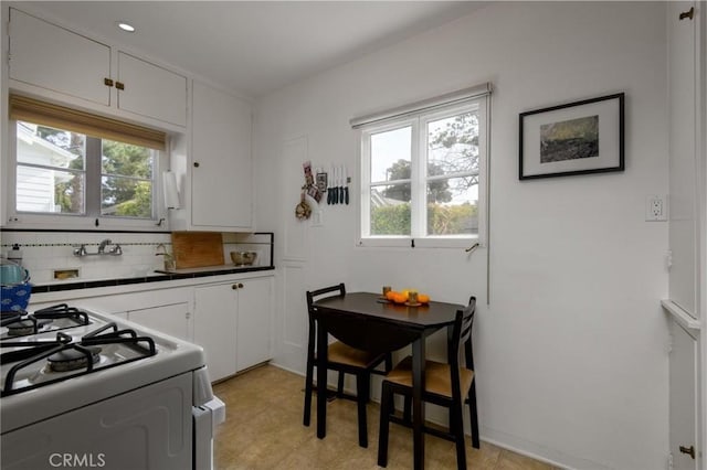 kitchen with gas range gas stove, light floors, white cabinets, and backsplash