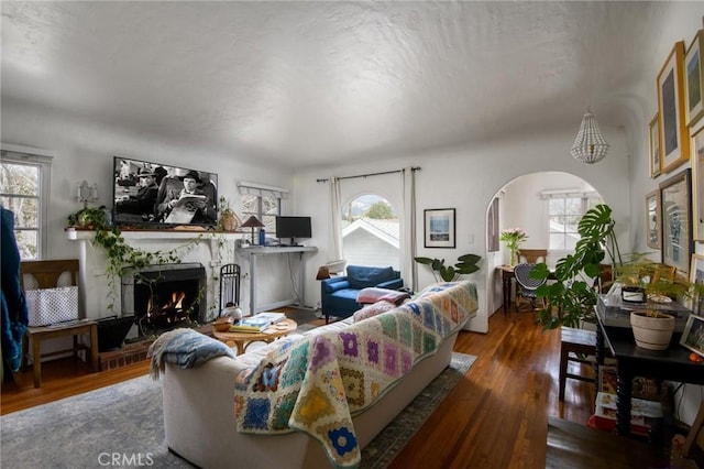 living room with arched walkways, a warm lit fireplace, and wood finished floors