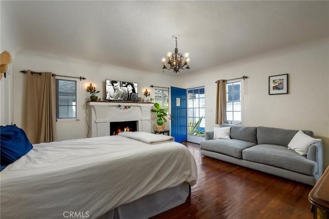 bedroom with a warm lit fireplace, access to exterior, a chandelier, and wood finished floors