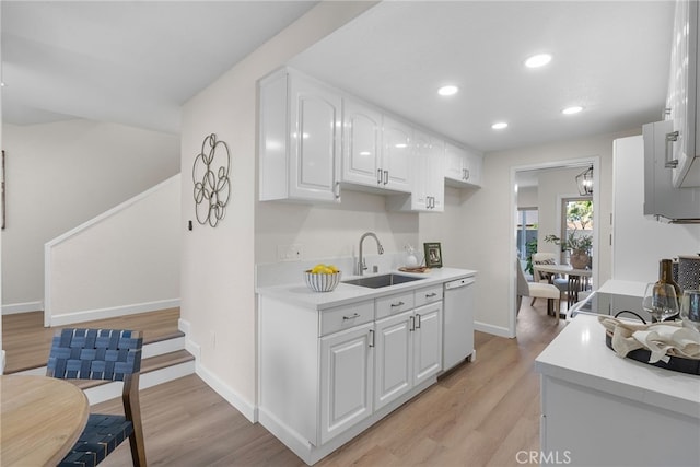 kitchen featuring white dishwasher, a sink, white cabinetry, light countertops, and light wood-type flooring