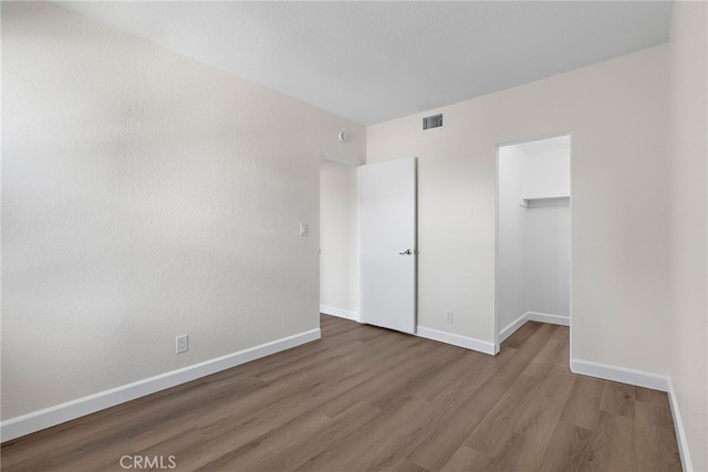 unfurnished bedroom with baseboards, visible vents, a walk in closet, and wood finished floors