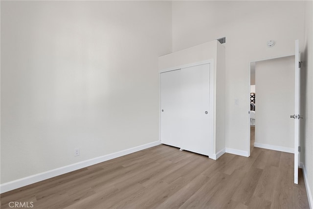 unfurnished bedroom featuring a high ceiling, wood finished floors, visible vents, and baseboards