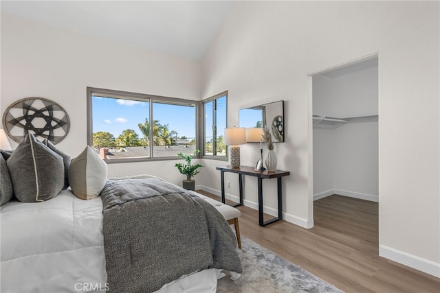 bedroom featuring high vaulted ceiling, a walk in closet, baseboards, and wood finished floors