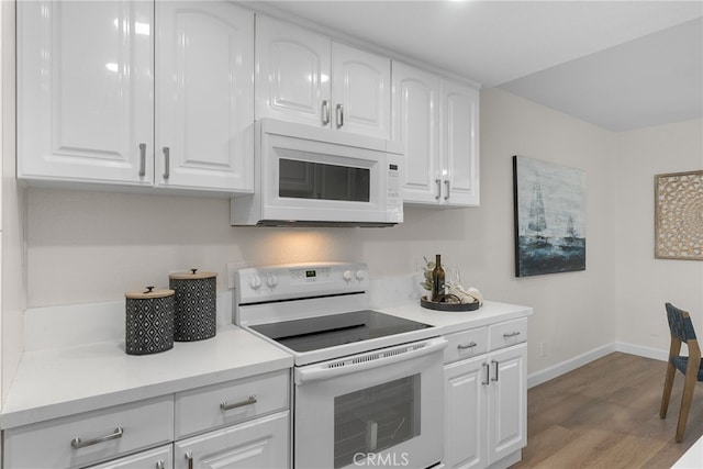 kitchen with baseboards, white appliances, wood finished floors, and white cabinets