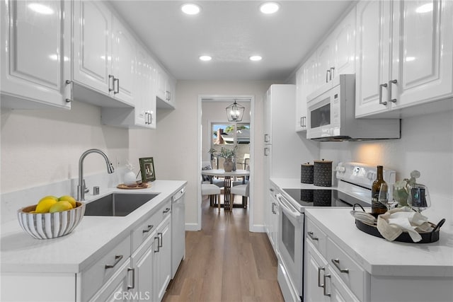 kitchen featuring electric range, white microwave, white cabinets, a sink, and wood finished floors