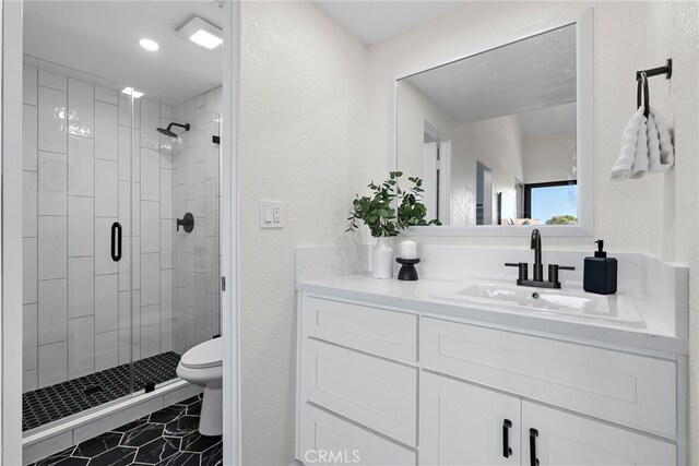 bathroom with a textured wall, vanity, a shower stall, and toilet