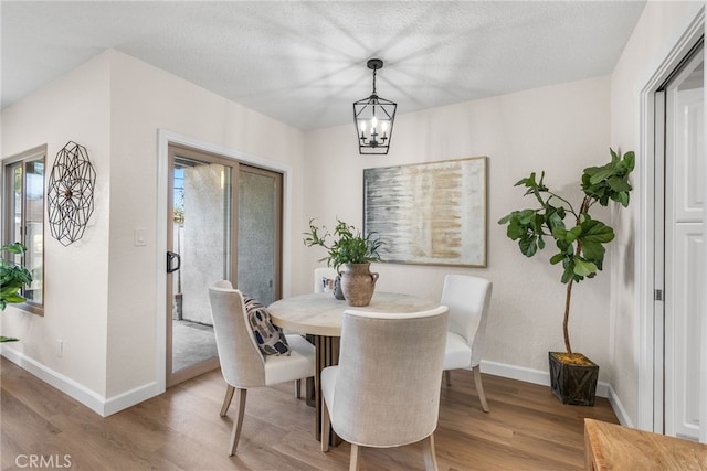 dining room with a textured ceiling, an inviting chandelier, wood finished floors, and baseboards