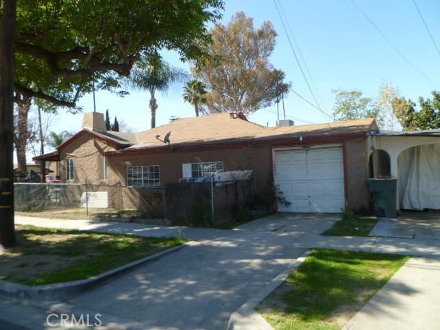 view of front of property with a chimney, stucco siding, fence, a garage, and driveway