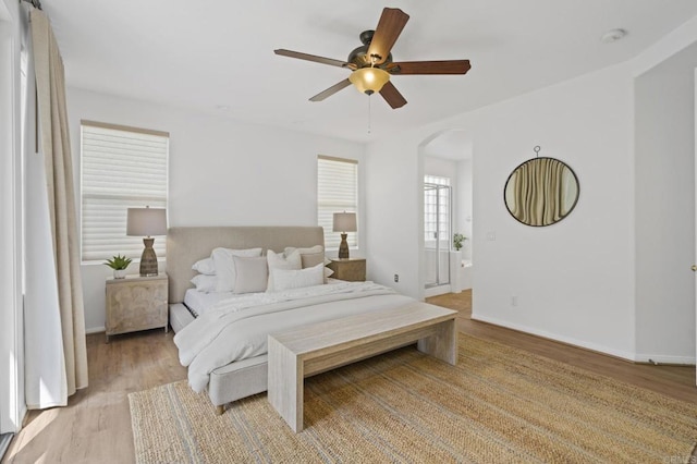 bedroom with light wood-type flooring, arched walkways, ceiling fan, and baseboards