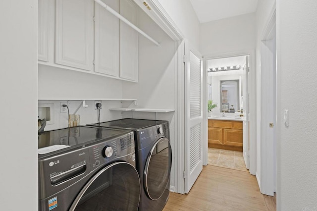 laundry area featuring washer and clothes dryer, a sink, cabinet space, and light wood-style floors