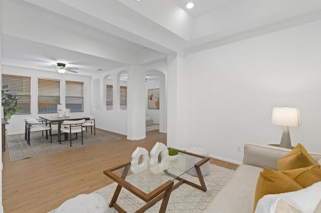 living area with arched walkways, wood finished floors, a ceiling fan, and baseboards