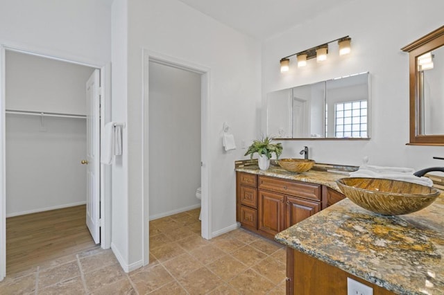 full bath featuring toilet, double vanity, a walk in closet, and a sink