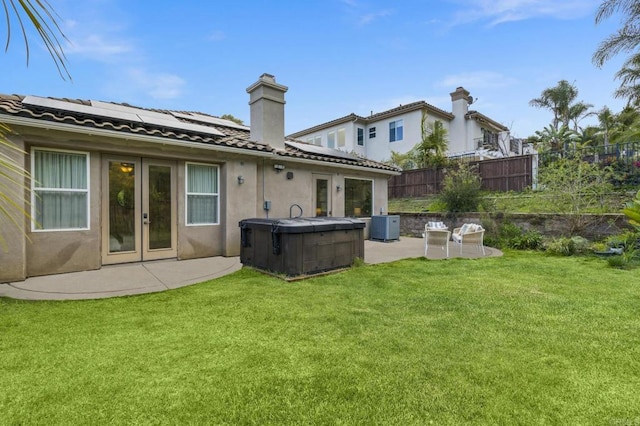 rear view of property featuring a hot tub, a lawn, solar panels, fence, and a patio area