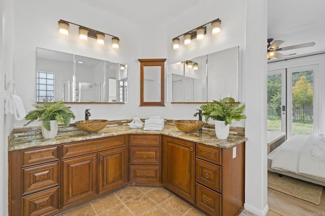 ensuite bathroom with double vanity, a sink, a ceiling fan, and a shower stall