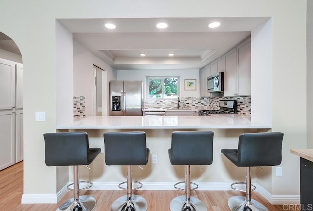 kitchen featuring a tray ceiling, stainless steel appliances, light countertops, decorative backsplash, and a sink