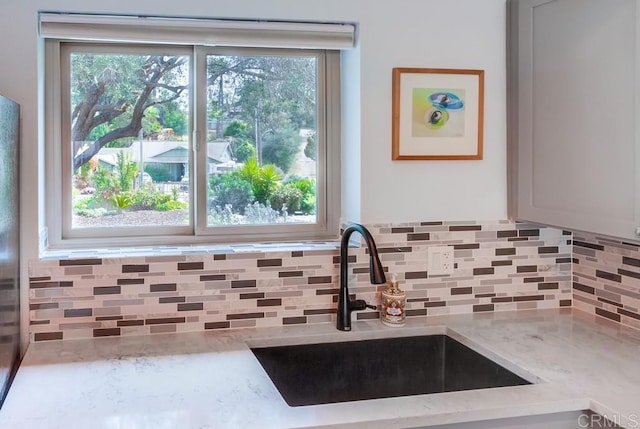 details featuring a sink, decorative backsplash, and light stone countertops