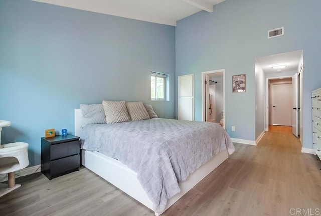 bedroom featuring visible vents, a high ceiling, wood finished floors, beamed ceiling, and baseboards