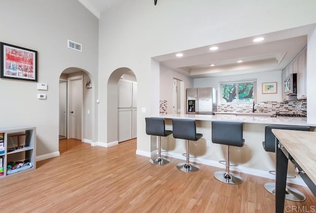 kitchen with a breakfast bar area, stainless steel appliances, arched walkways, and a raised ceiling