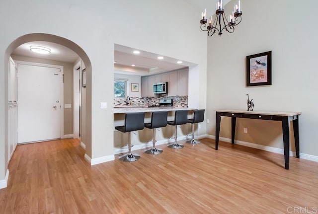 kitchen featuring arched walkways, stainless steel appliances, a breakfast bar, light wood finished floors, and a raised ceiling