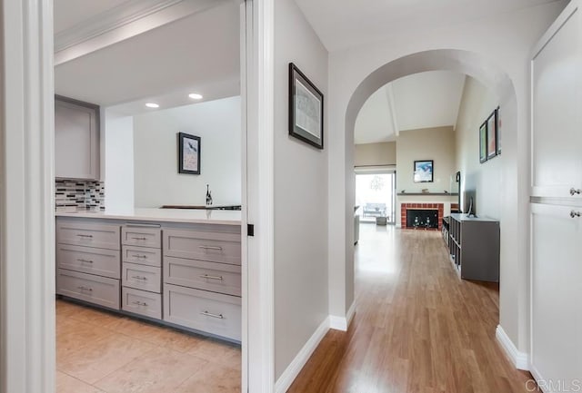 hallway featuring arched walkways, light wood-style flooring, and baseboards