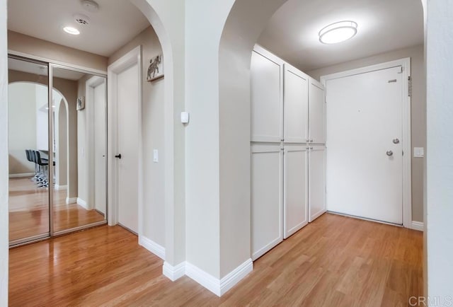 hallway with arched walkways, baseboards, and light wood-style floors