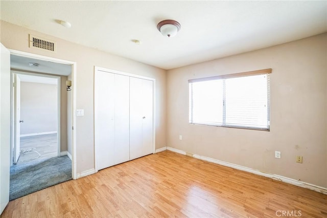 unfurnished bedroom with light wood-type flooring, a closet, visible vents, and baseboards