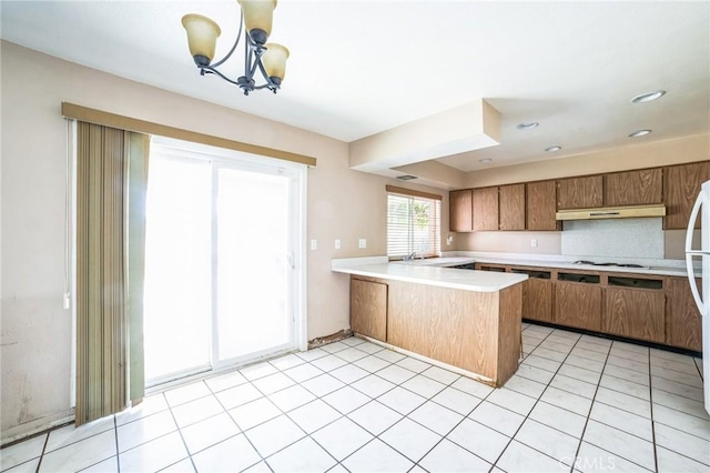 kitchen featuring white stovetop, brown cabinets, a peninsula, light countertops, and under cabinet range hood