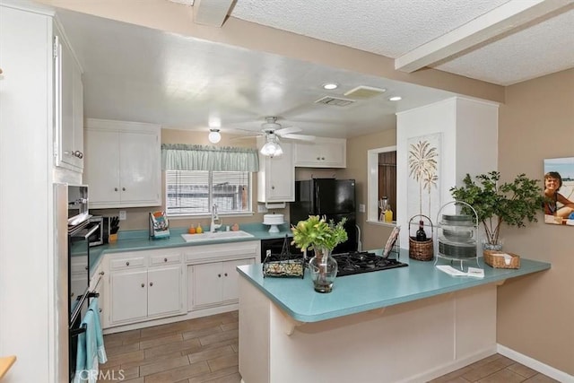 kitchen with wood finish floors, black appliances, a sink, a peninsula, and white cabinets