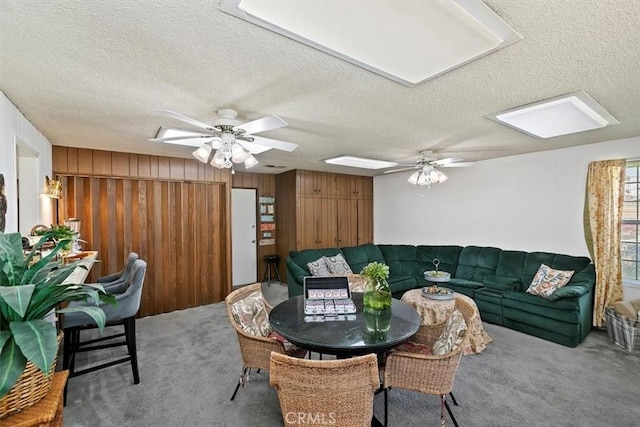 carpeted living area with wooden walls, a textured ceiling, and ceiling fan