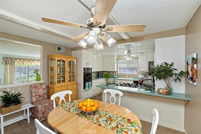 dining room with wood finished floors, a ceiling fan, visible vents, and a textured ceiling