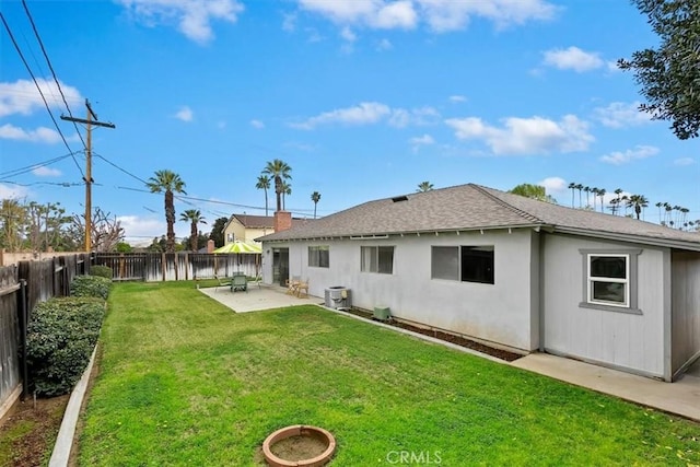 rear view of property featuring a patio, a yard, a fenced backyard, a shingled roof, and central air condition unit