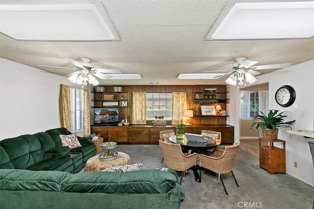 carpeted living room with a textured ceiling, ceiling fan, and wooden walls