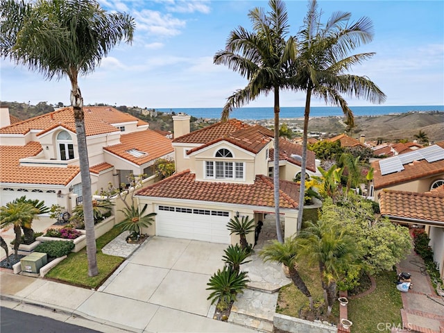 view of front of house with stucco siding, concrete driveway, a garage, a water view, and a tile roof