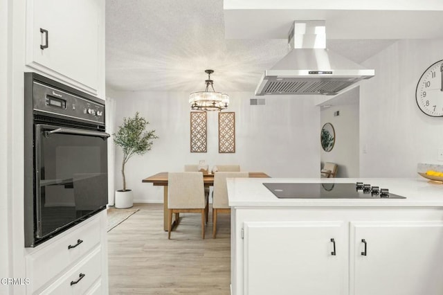 kitchen featuring a peninsula, black appliances, wall chimney exhaust hood, and white cabinetry