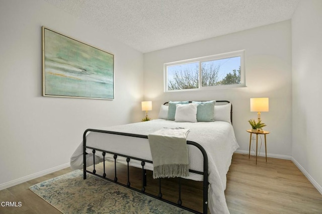 bedroom featuring baseboards, a textured ceiling, and wood finished floors