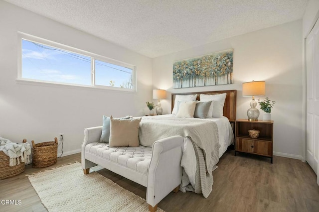 bedroom with a textured ceiling, baseboards, and wood finished floors