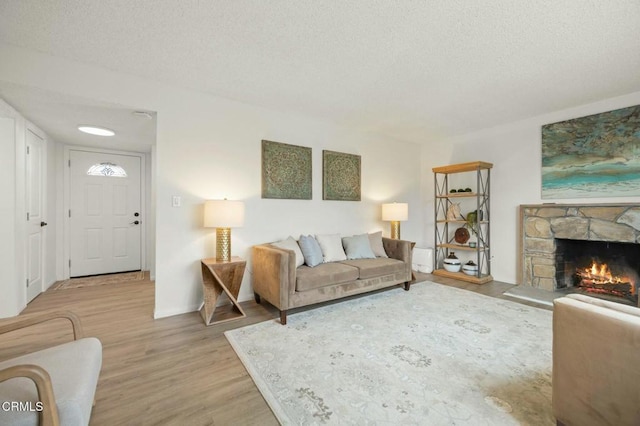 living area featuring a stone fireplace, baseboards, light wood-type flooring, and a textured ceiling