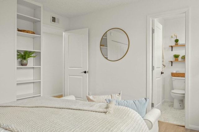 bedroom featuring visible vents, baseboards, wood finished floors, a textured ceiling, and ensuite bath