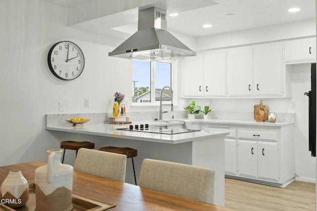 kitchen with range hood, a breakfast bar, a peninsula, white cabinets, and black electric stovetop