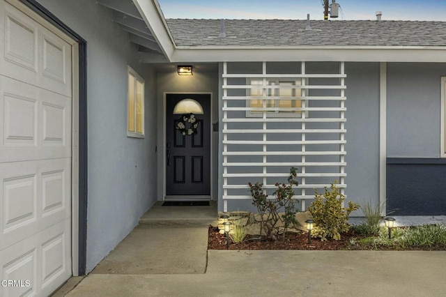 property entrance with stucco siding, a garage, and roof with shingles