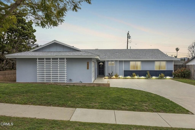 single story home featuring a shingled roof, a front lawn, fence, and stucco siding