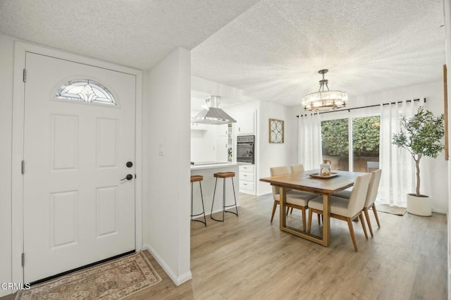 foyer featuring a notable chandelier, baseboards, light wood-style floors, and a textured ceiling