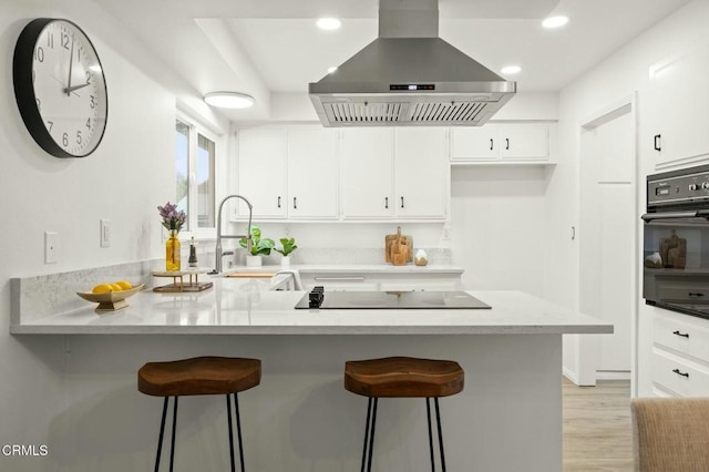 kitchen with black appliances, a sink, white cabinetry, a peninsula, and wall chimney range hood